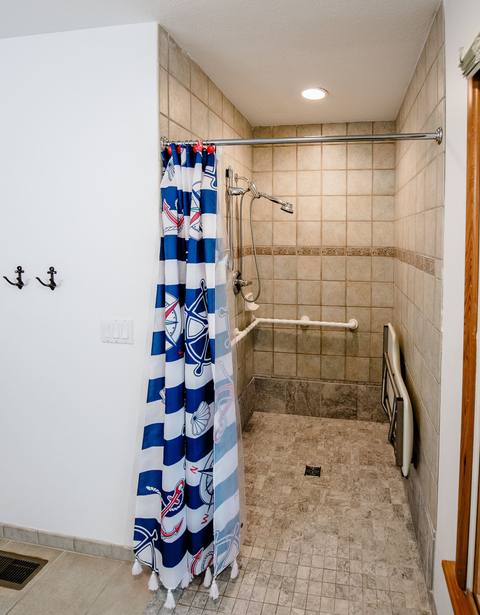 Curbless roll-in shower with grab bars, a hand-held wand, and a fold-down seat