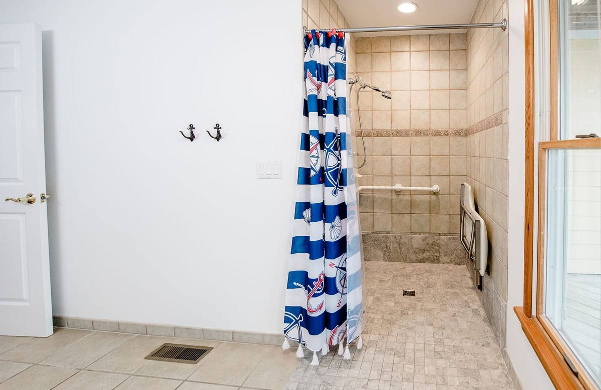 Wide view of the accessible shower with a window, grab bars, and a fold-down seat