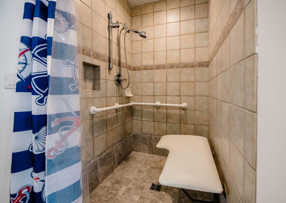 Curbless tile shower with grab bars, a hand-held wand, and a fold-down seat