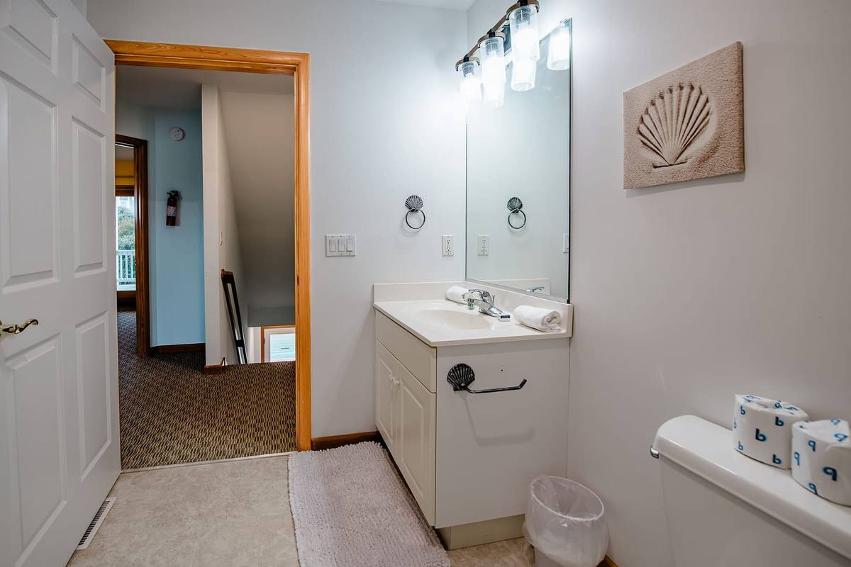 Bathroom with a single vanity and a shell picture, and a hallway beyond
