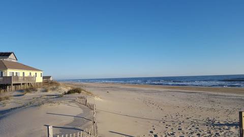 Dune fencing casting long shadows on the sand above an empty beach and open ocean