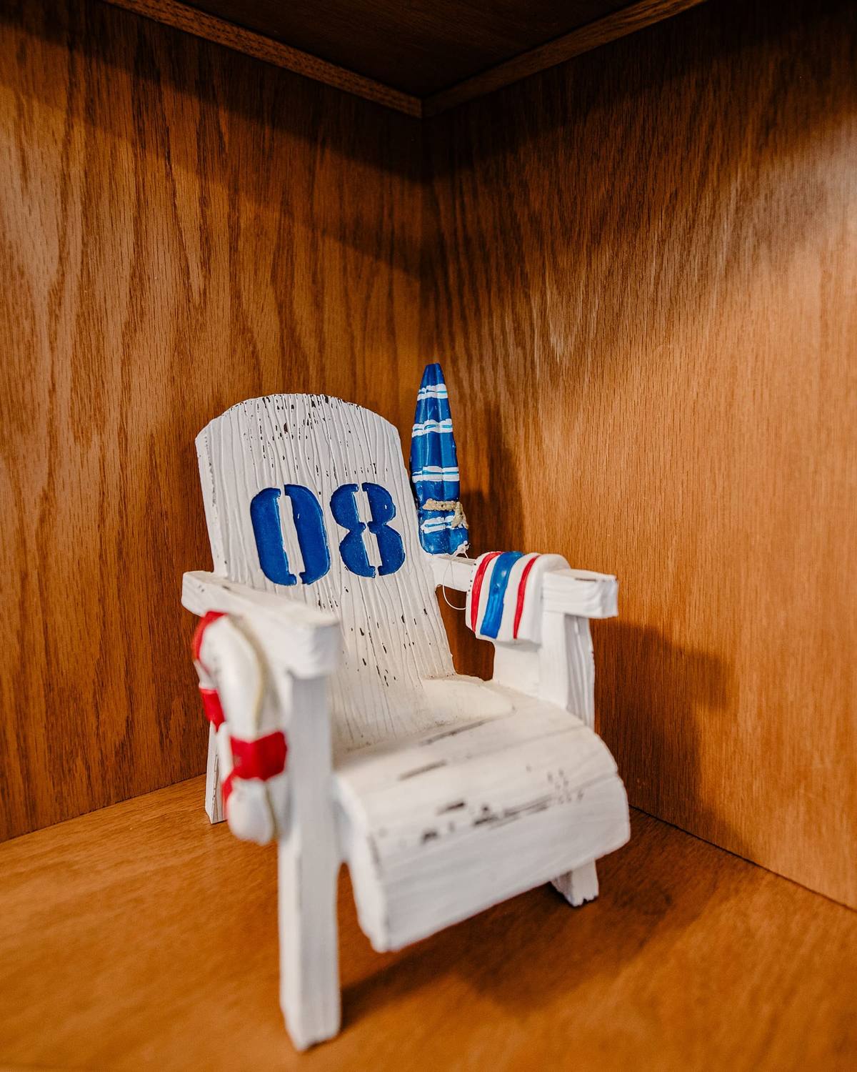A small white Adirondack chair figurine numbered 08 on a wood shelf