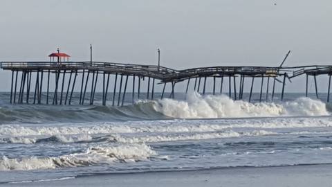 Large breaking waves beside a wooden fishing pier on a cloudy day