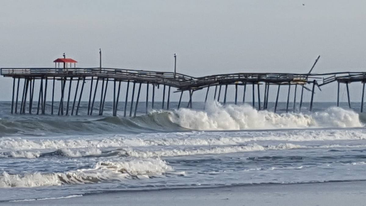 Large breaking waves beside a wooden fishing pier on a cloudy day