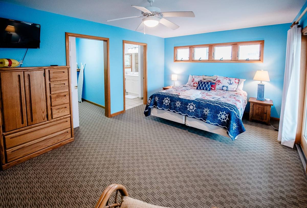 Blue bedroom with a king bed, armoire with a TV, and a doorway to the bath