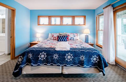 Bright blue bedroom with a king bed in a nautical quilt and deck access