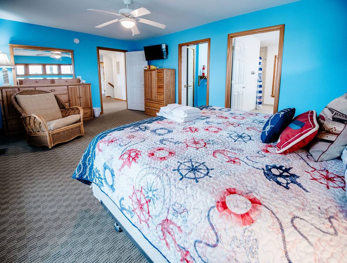 Bed with a red, white, and blue nautical quilt and a wicker chair in the corner