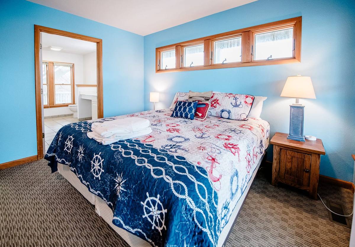 King bed with a navy ship-wheel quilt, lamps, and a row of transom windows above