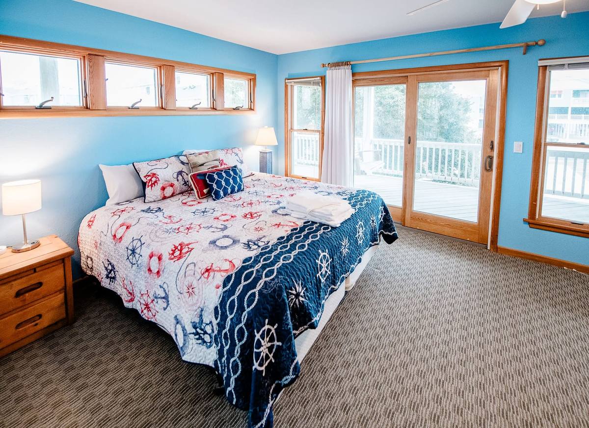 Blue bedroom with a bed, nightstand, and glass doors to the deck