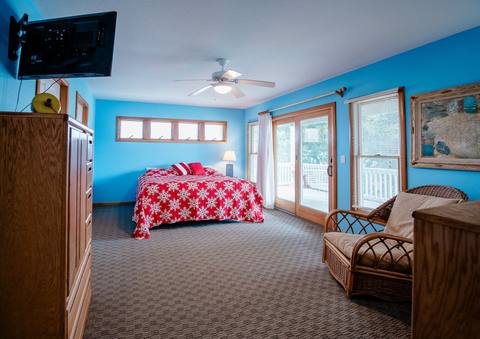 Blue bedroom with a king bed in a red-and-white snowflake quilt, facing glass doors that open to a deck