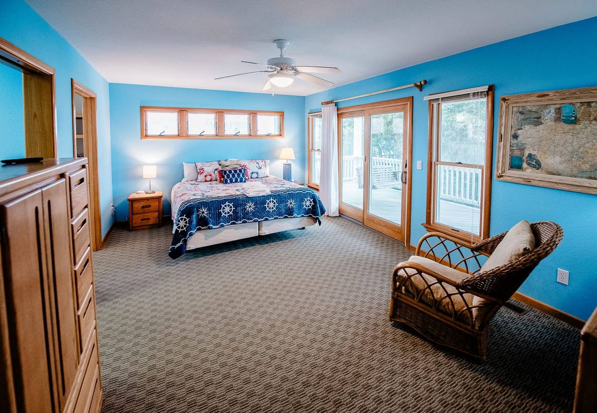 Wide view of the blue bedroom with a ceiling fan, wicker chair, and armoire