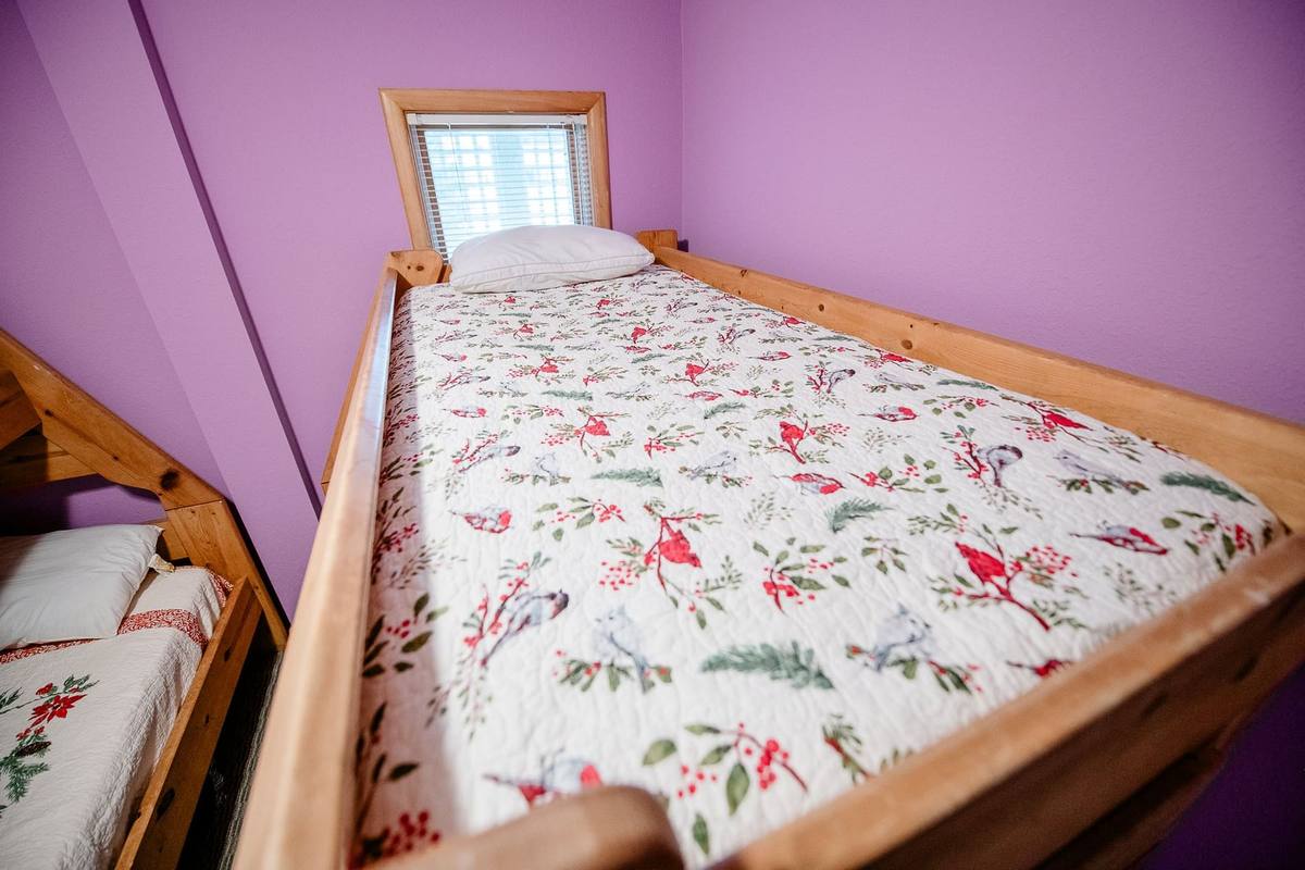 Wood bunk beds dressed in a cardinal-and-holly print quilt, with a poinsettia quilt visible on the bunk below, in a lavender-walled bedroom