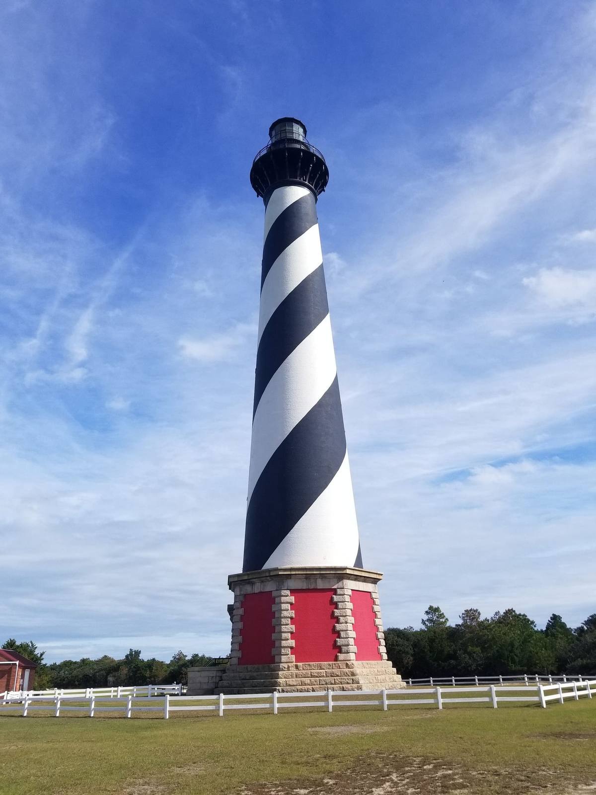 Looking up at the black-and-white spiral tower of the Cape Hatteras Lighthouse against blue sky and clouds