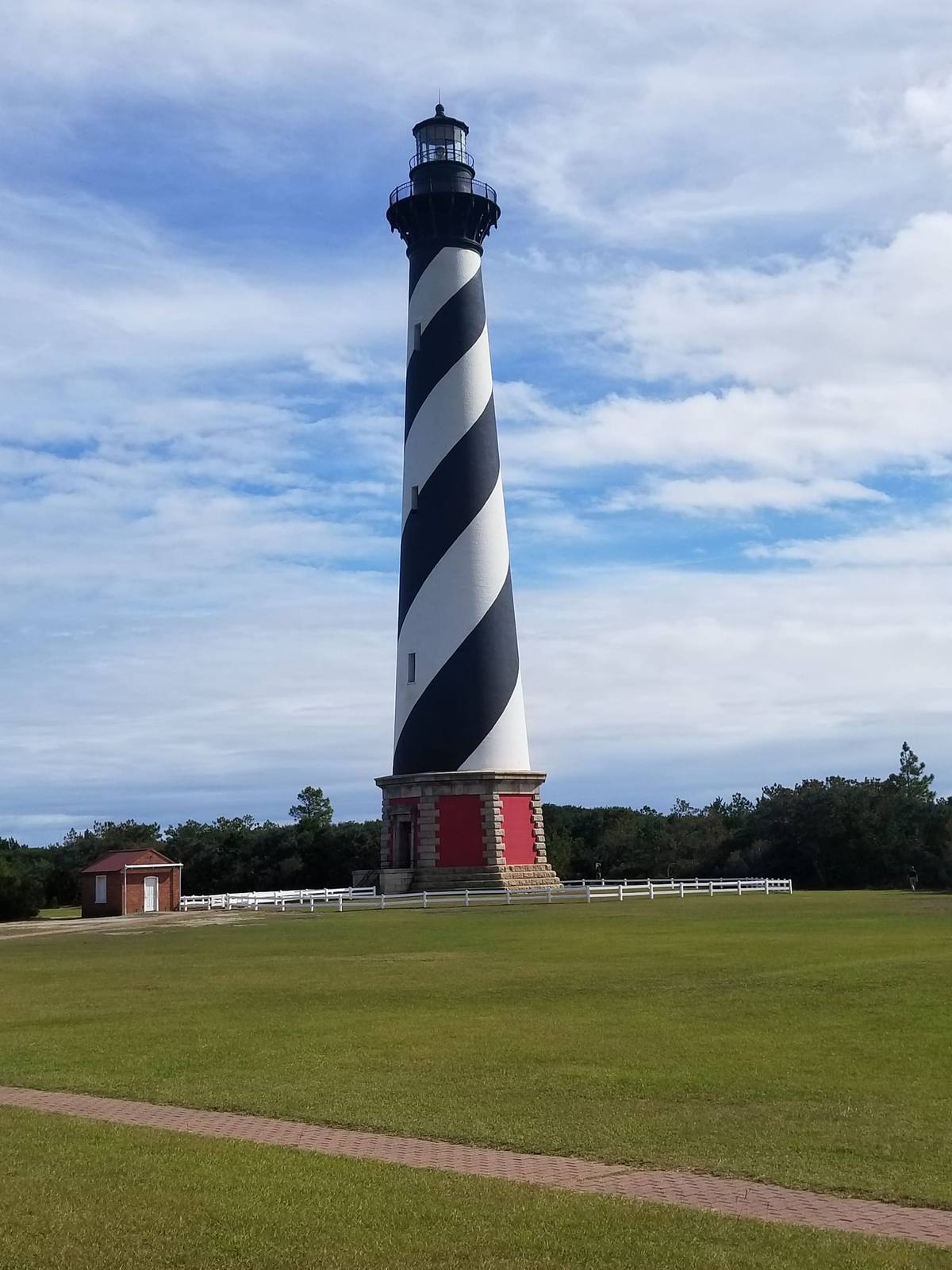The black-and-white spiral-striped Cape Hatteras Lighthouse rising above a grassy lawn under a blue sky