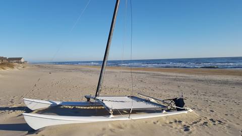 A small catamaran sailboat resting on the beach with the ocean behind it