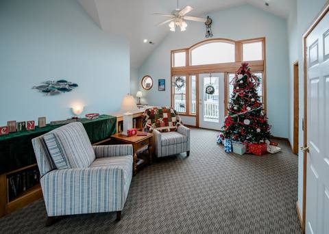 A decorated Christmas tree strung with red and silver ornaments and wrapped gifts underneath, standing beside the front door in the great room