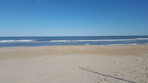 A wide, empty beach meeting a calm ocean under a clear blue sky