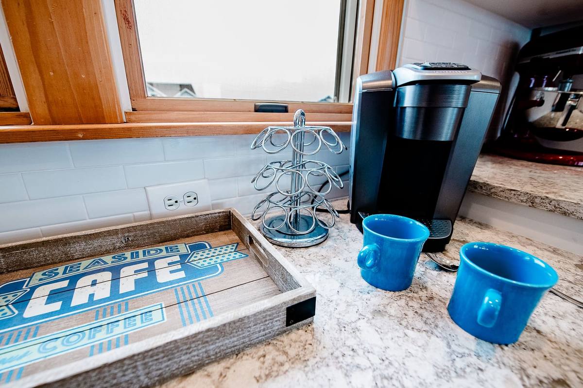 Single-cup coffee maker and blue mugs on the granite counter beside a Seaside Cafe tray