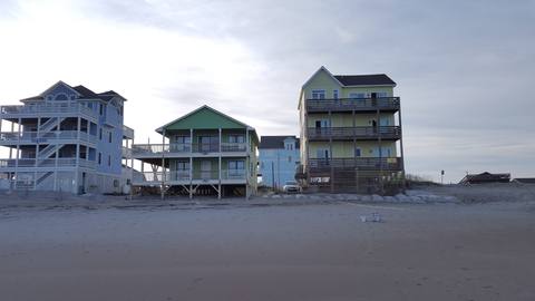 Green and yellow beachfront cottages on stilts seen from the sand