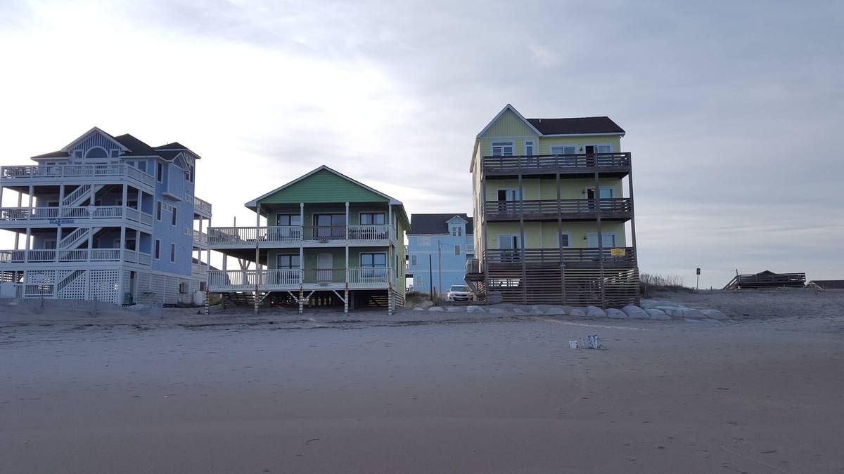 Green and yellow beachfront cottages on stilts seen from the sand