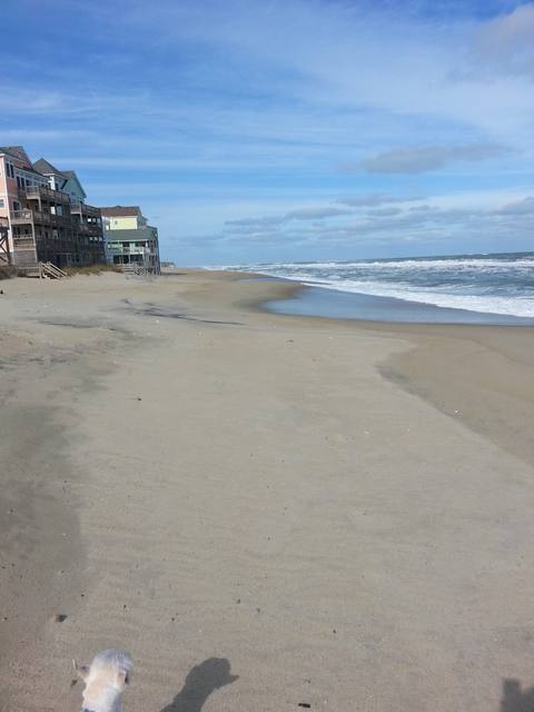 An empty beach with a row of beach cottages in the distance under a clear sky