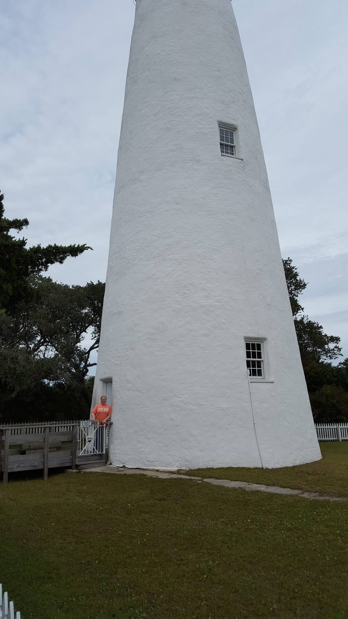 Looking up at the red-brick Currituck Beach Lighthouse from its base, framed by trees