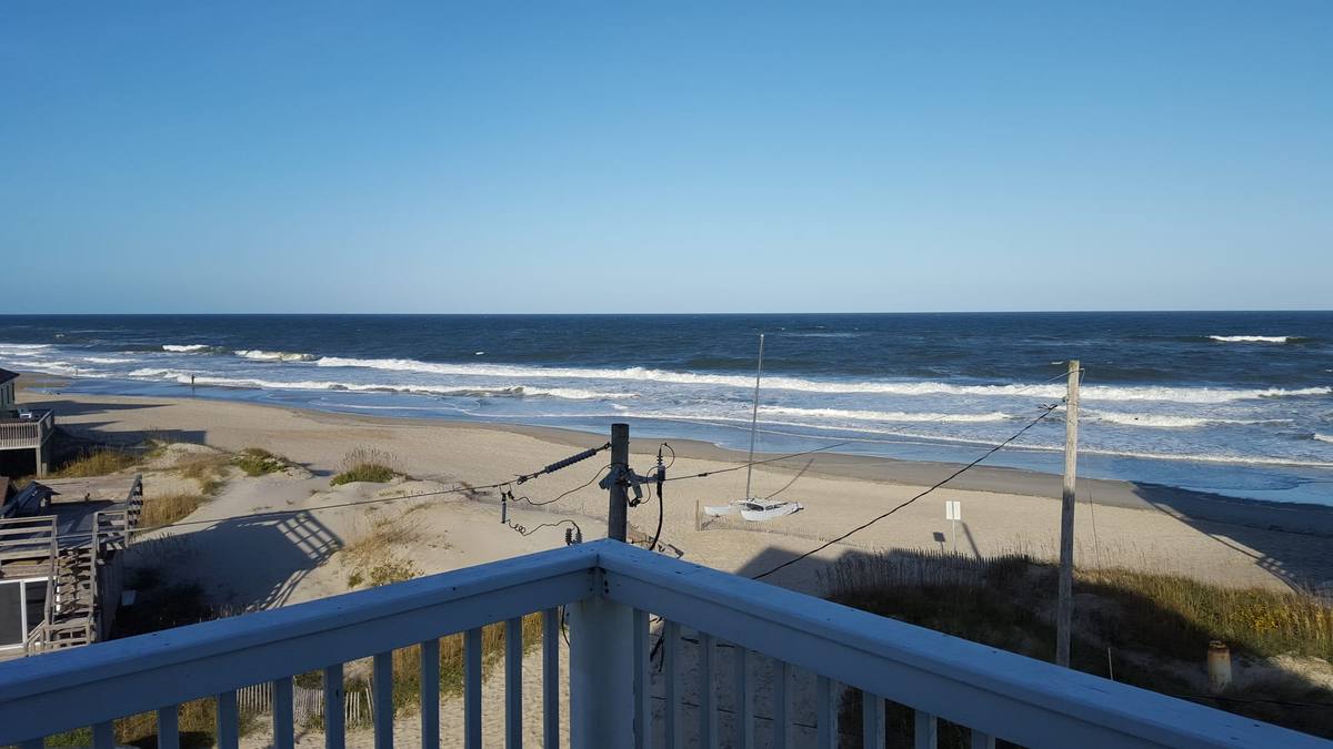 View toward the beach and a small sailboat from a covered deck railing