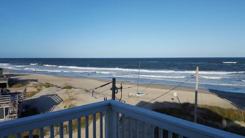 View toward the beach and a small sailboat from a covered deck railing
