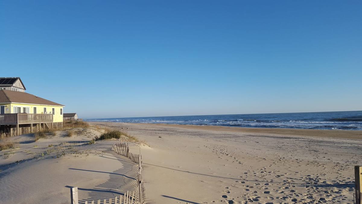 A sandy path through dune fencing leading toward the ocean
