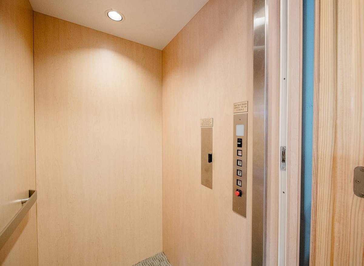 Wood-paneled elevator interior with a call panel and handrail