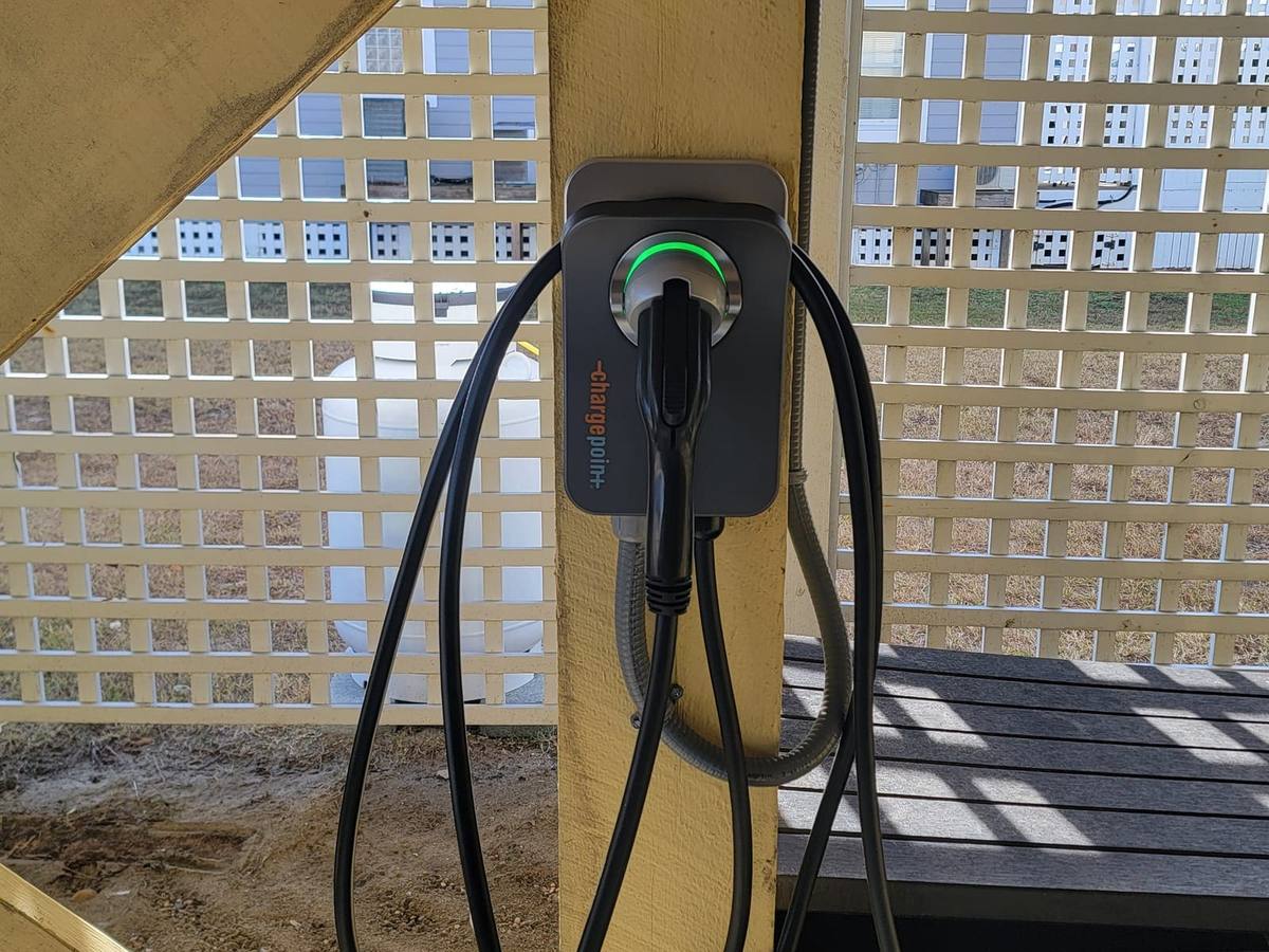 A wall-mounted EV charger with its cable coiled, mounted on a lattice wall