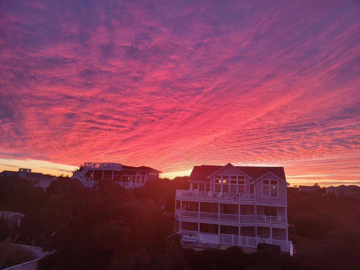 A fiery red and magenta sky at sunset behind silhouetted beach houses