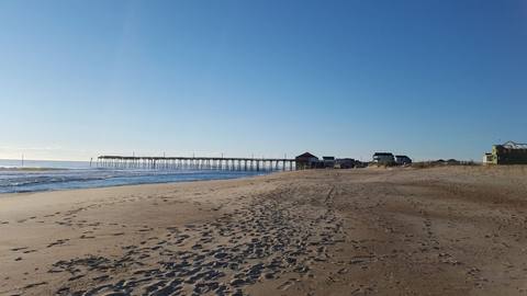 A long fishing pier reaching into the surf beyond an empty beach in early light