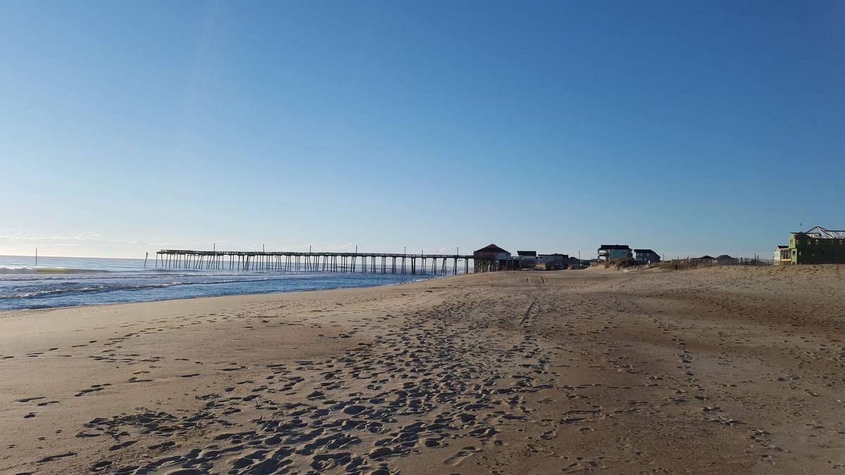 A long fishing pier reaching into the surf beyond an empty beach in early light