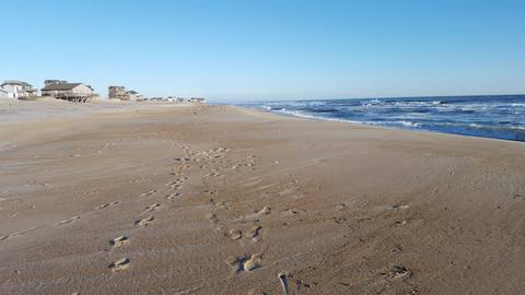 Footprints across a wide, empty beach leading toward the surf line with houses in the distance