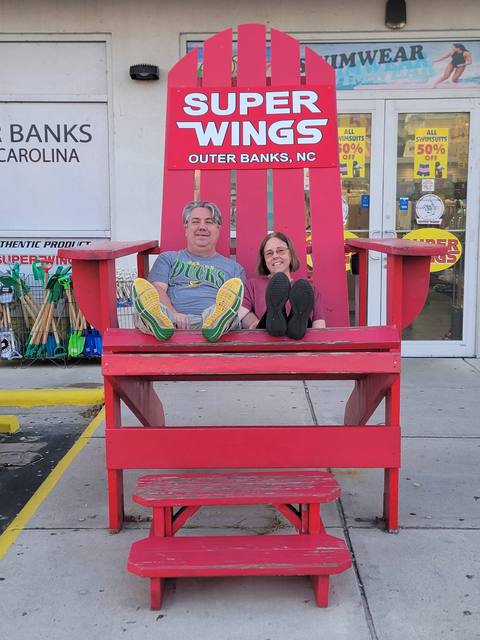 A couple sitting in a giant red Adirondack chair outside an Outer Banks shop