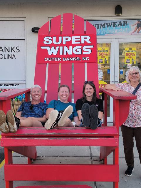 A group of women laughing together in a giant red Adirondack chair outside a shop
