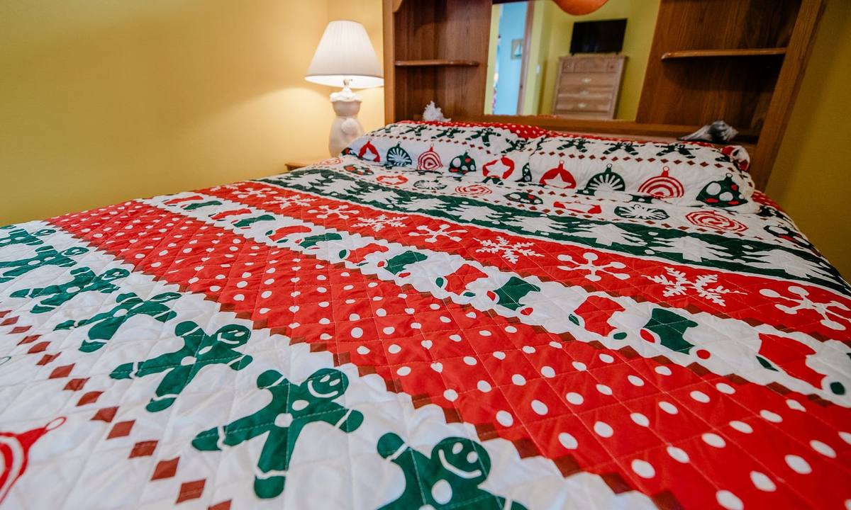 Close-up of a red, white, and green quilt patterned with gingerbread men, snowflakes, and mini stockings