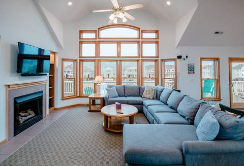 Top-level great room with the gas fireplace lit, a vaulted ceiling, and a full wall of windows