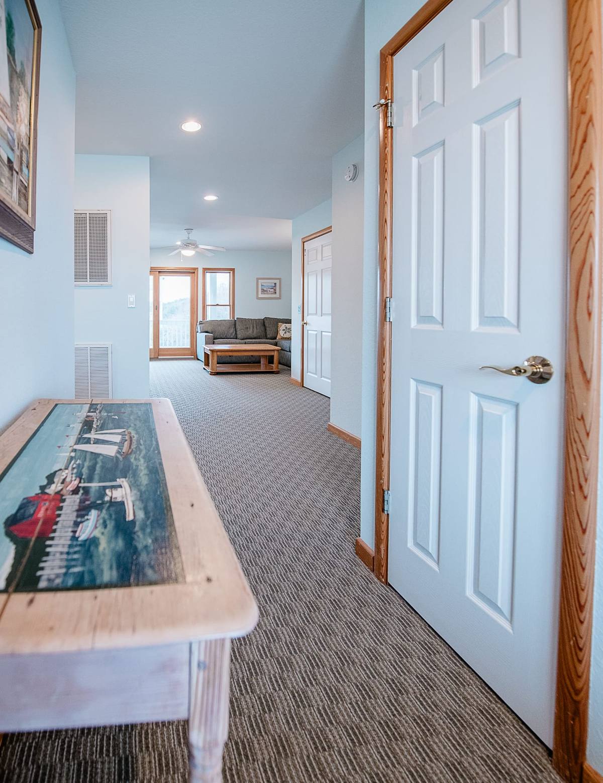 Hallway with a sailboat painting on a wood console and the den in the distance