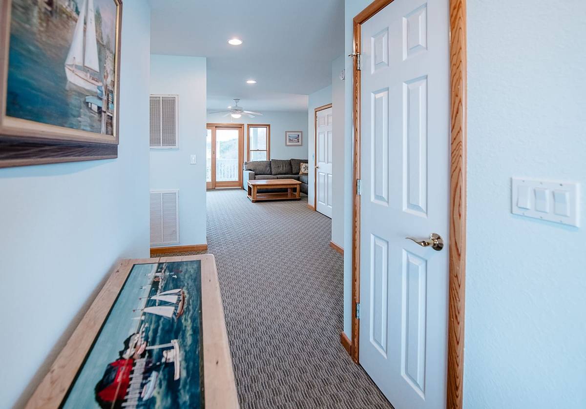 Carpeted hallway with framed sailboat art leading to the den