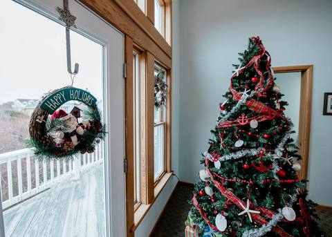 A Happy Holidays wreath with a snowman figure hangs on the glass deck door, with the fully decorated Christmas tree standing just inside