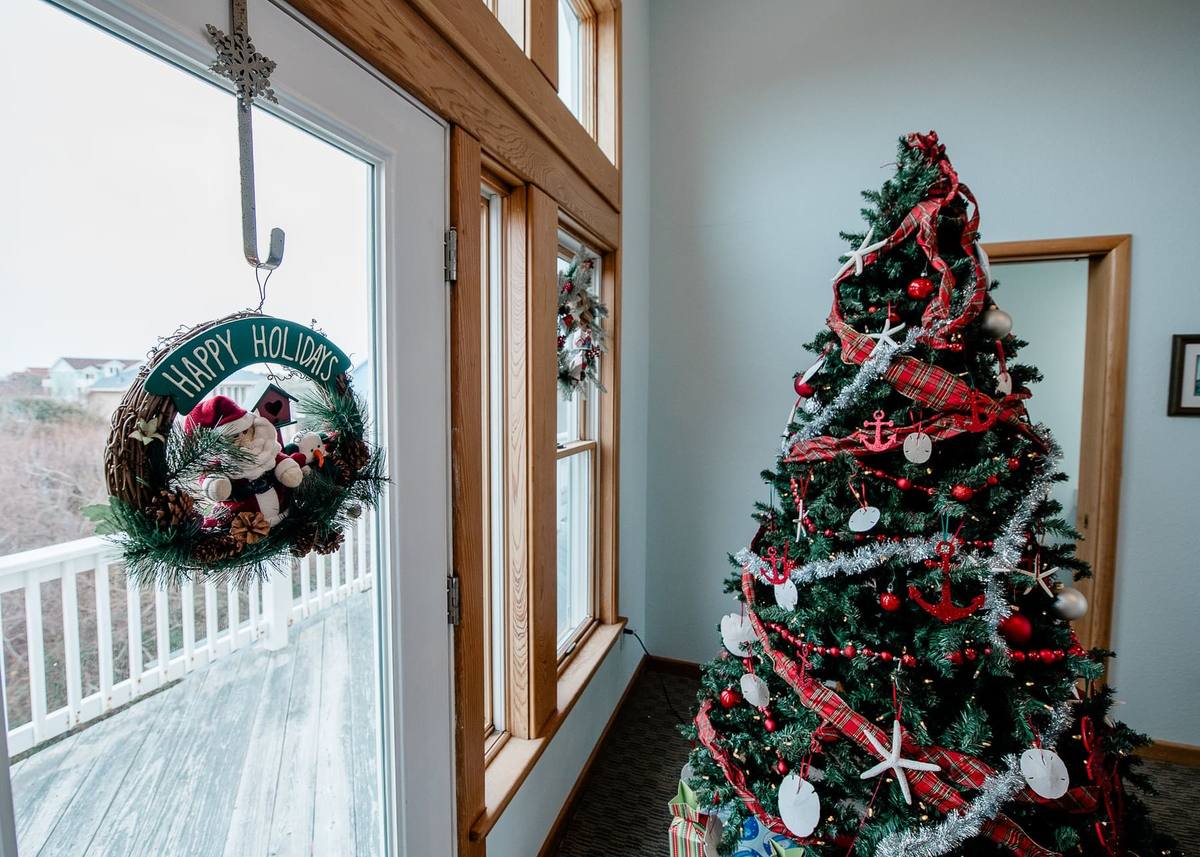 A Happy Holidays wreath with a snowman figure hangs on the glass deck door, with the fully decorated Christmas tree standing just inside