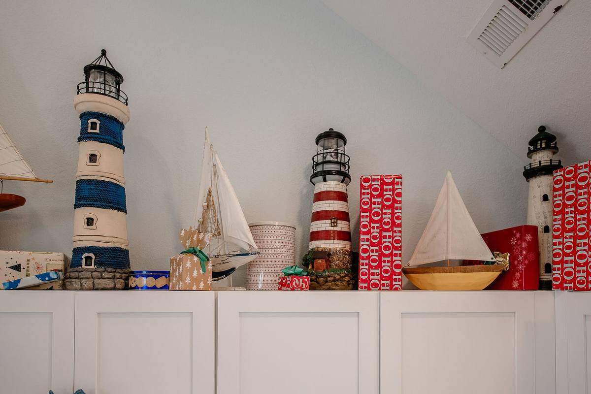 Red-wrapped gift boxes printed with HO HO HO arranged atop white kitchen cabinets alongside model lighthouses and sailboats