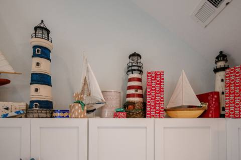Red-wrapped gift boxes printed with HO HO HO arranged atop white kitchen cabinets alongside model lighthouses and sailboats