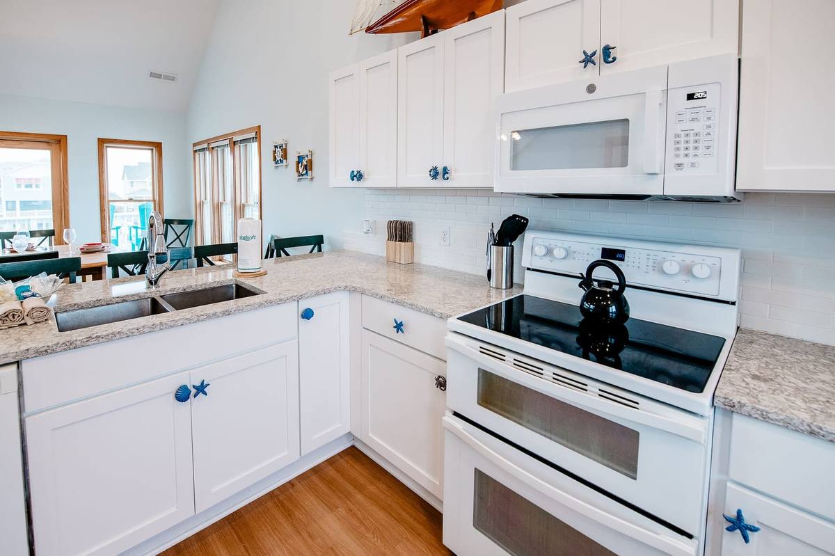 White double oven and glass cooktop with a microwave above and blue cabinet knobs