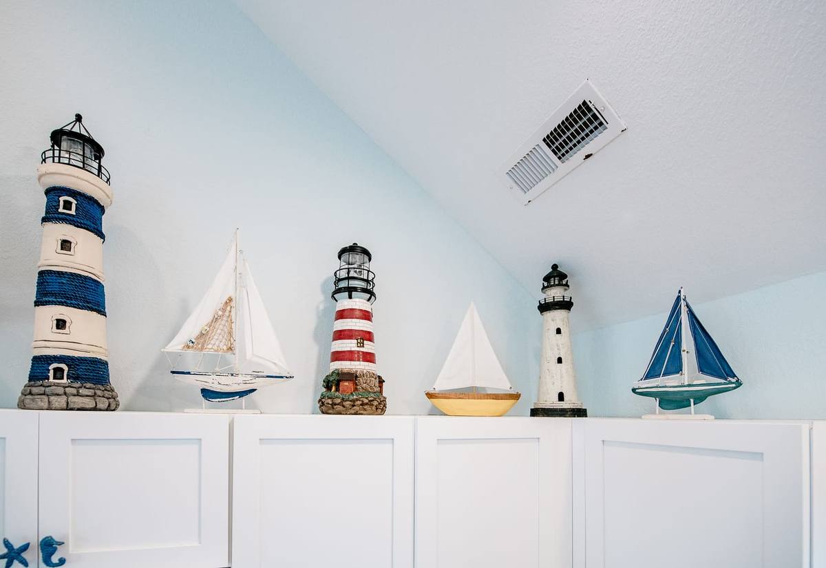 Decorative lighthouses and sailboats lined up on top of the kitchen cabinets