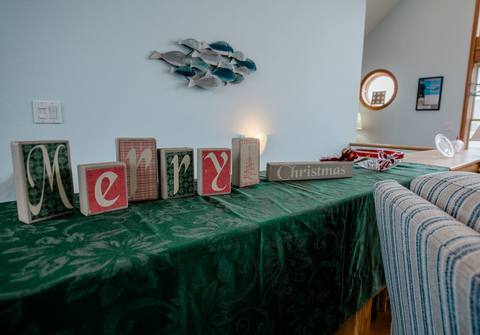 Wood block letters spelling Merry Christmas arranged on a green table runner near a coastal fish sculpture