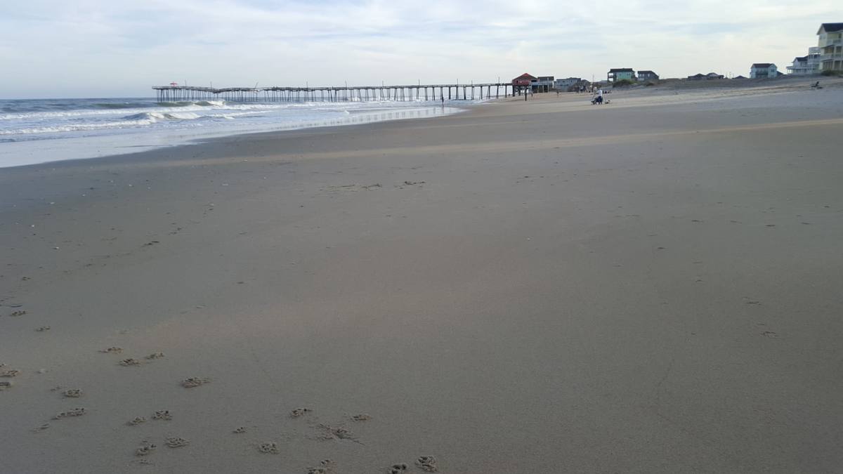 An empty beach in soft afternoon light with a fishing pier in the distance