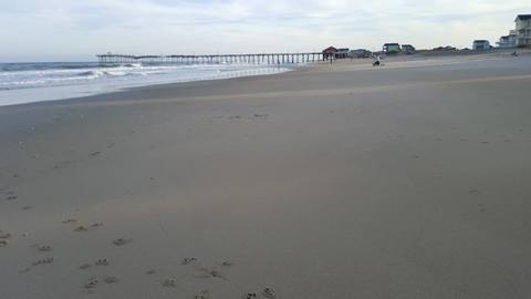 An empty beach in soft afternoon light with a fishing pier in the distance